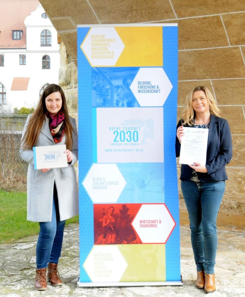Dieses Bild zeigt Katharina Wiener (Regionalmanagerin) und Nicole Graf (Projektkoordinatorin) mit dem Roll-Up des Leitbilds.